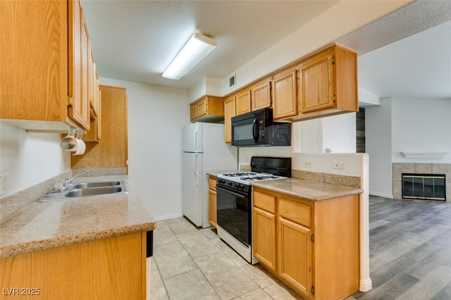 kitchen with a tile fireplace, sink, white fridge, range with gas stovetop, and a textured ceiling