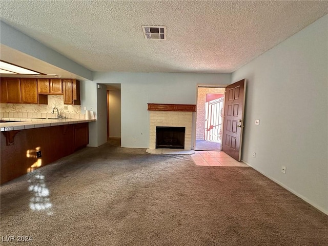 unfurnished living room featuring a textured ceiling, sink, light carpet, and a tiled fireplace