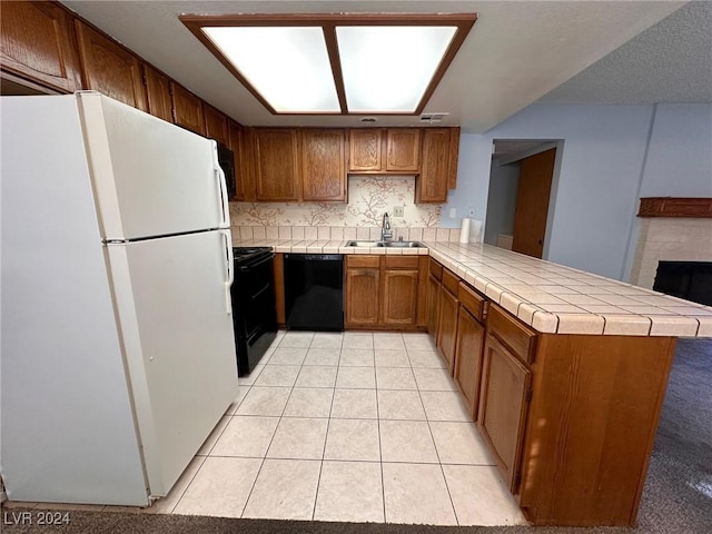 kitchen with sink, backsplash, kitchen peninsula, a tiled fireplace, and black appliances