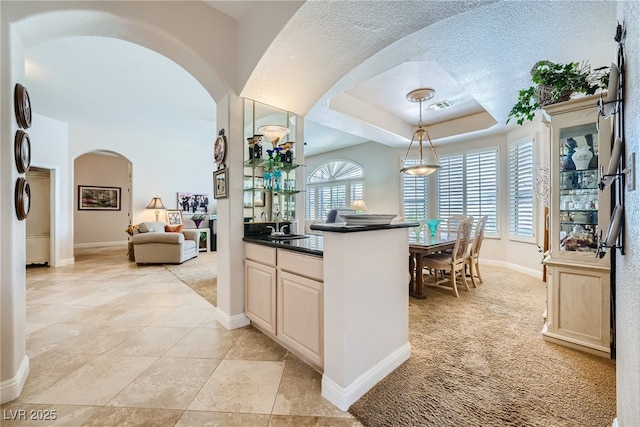 kitchen with sink, light colored carpet, pendant lighting, a textured ceiling, and a tray ceiling