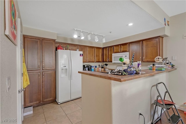 kitchen with a kitchen breakfast bar, kitchen peninsula, light tile patterned floors, and white appliances