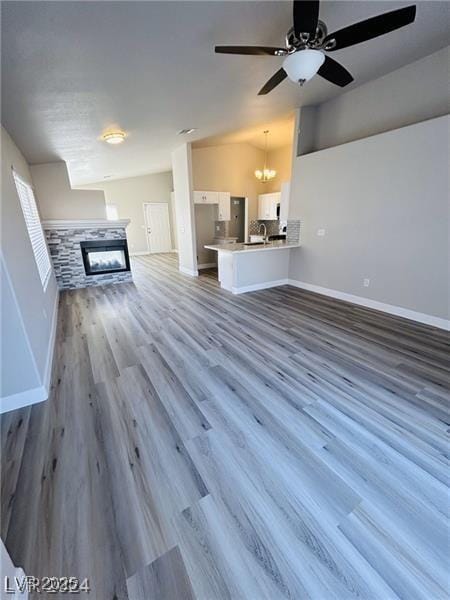 unfurnished living room with wood-type flooring, a fireplace, and ceiling fan with notable chandelier