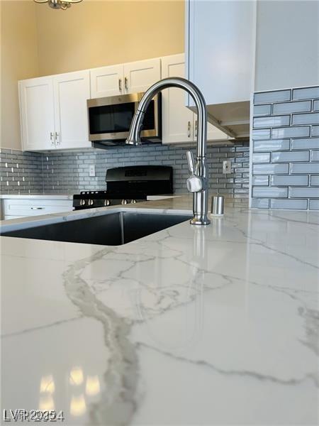 room details featuring tasteful backsplash, light stone counters, gas stove, and white cabinetry