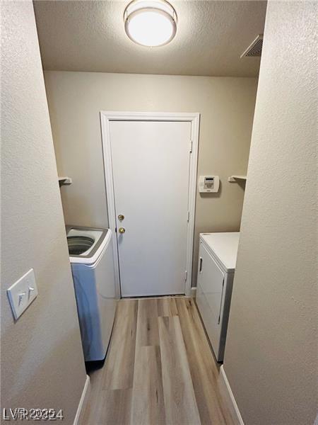 laundry area with independent washer and dryer, a textured ceiling, and light hardwood / wood-style flooring