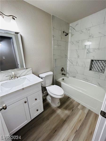 full bathroom with toilet, tiled shower / bath combo, hardwood / wood-style floors, and vanity