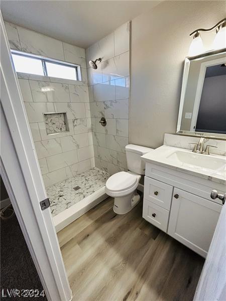 bathroom featuring hardwood / wood-style flooring, tiled shower, vanity, and toilet