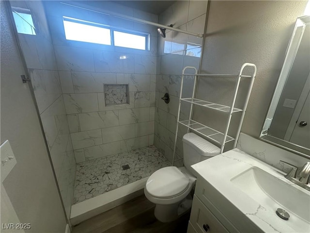 bathroom with a wealth of natural light, tiled shower, vanity, and toilet