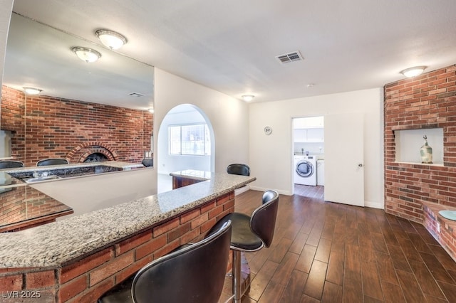 bar featuring dark hardwood / wood-style floors, washing machine and dryer, light stone counters, and brick wall