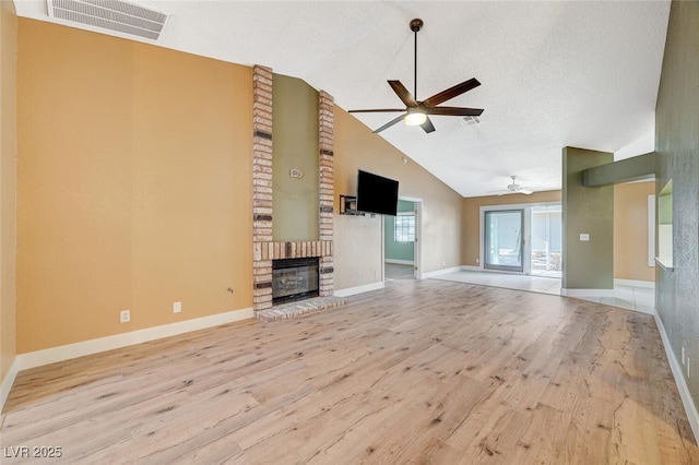 unfurnished living room featuring lofted ceiling, a brick fireplace, light hardwood / wood-style flooring, ceiling fan, and a textured ceiling