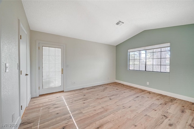 empty room featuring a textured ceiling, light hardwood / wood-style floors, and vaulted ceiling