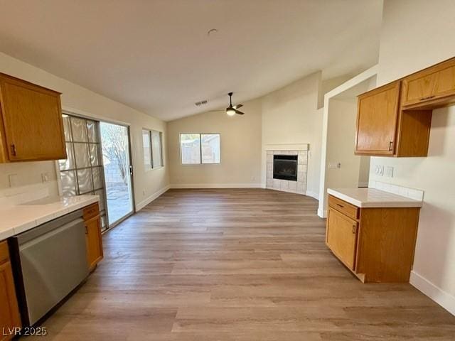 kitchen featuring ceiling fan, a tile fireplace, dishwasher, light hardwood / wood-style floors, and lofted ceiling