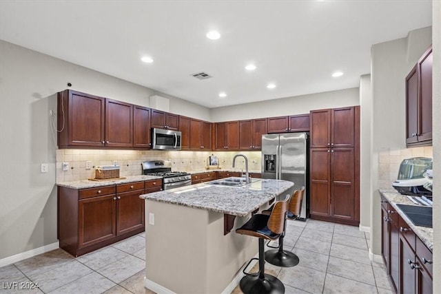 kitchen with a kitchen bar, light stone countertops, stainless steel appliances, sink, and an island with sink