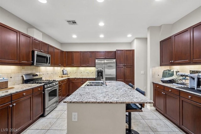 kitchen featuring a kitchen bar, light stone countertops, stainless steel appliances, a kitchen island with sink, and light tile patterned flooring