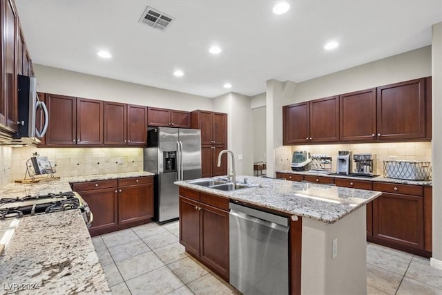 kitchen with appliances with stainless steel finishes, light stone counters, a kitchen island with sink, and sink