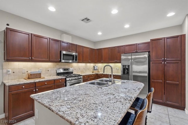 kitchen with light stone countertops, sink, an island with sink, a breakfast bar, and appliances with stainless steel finishes