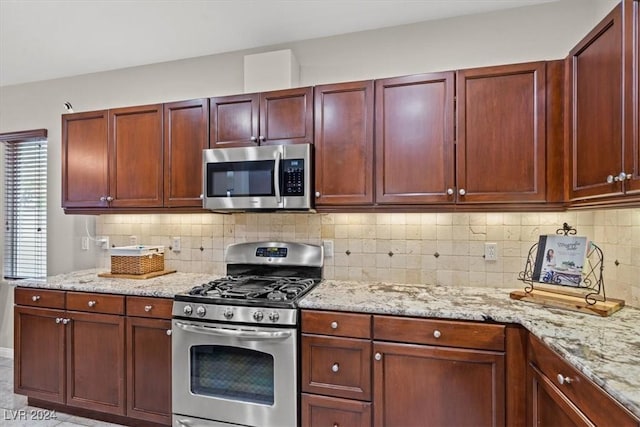 kitchen with light tile patterned flooring, light stone countertops, backsplash, and appliances with stainless steel finishes