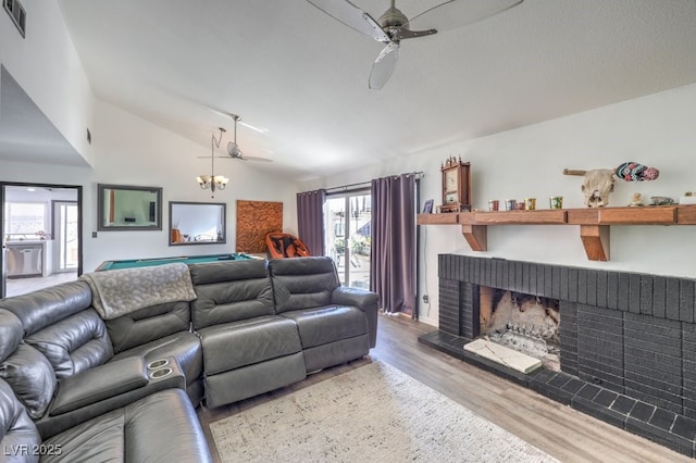 living room featuring ceiling fan, vaulted ceiling, a brick fireplace, and light wood-type flooring