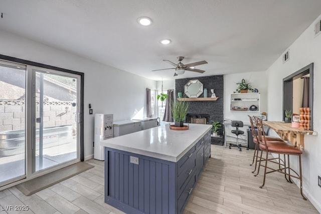 kitchen featuring ceiling fan, a kitchen island, a brick fireplace, and a wealth of natural light