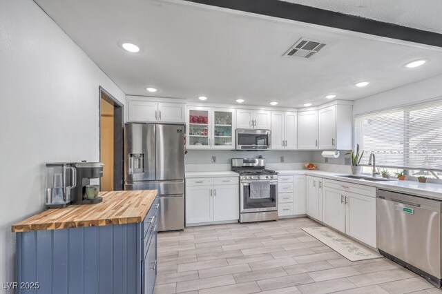 kitchen with wood counters, sink, beamed ceiling, white cabinetry, and stainless steel appliances