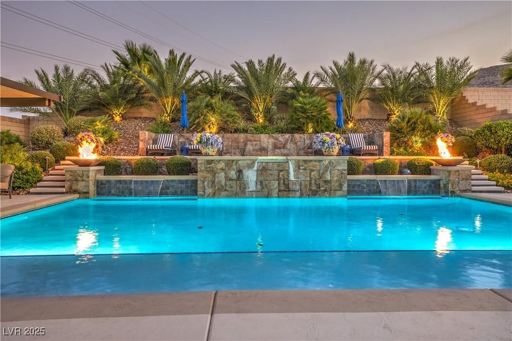 pool at dusk featuring pool water feature and an outdoor fire pit