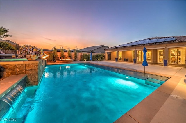 pool at dusk featuring pool water feature and a patio