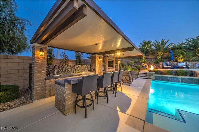 pool at dusk featuring pool water feature, a patio area, and a bar