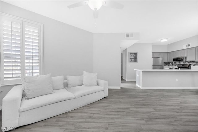 living room featuring ceiling fan, sink, and light hardwood / wood-style flooring