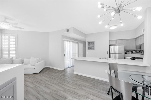 kitchen with kitchen peninsula, light hardwood / wood-style floors, sink, gray cabinets, and stainless steel refrigerator