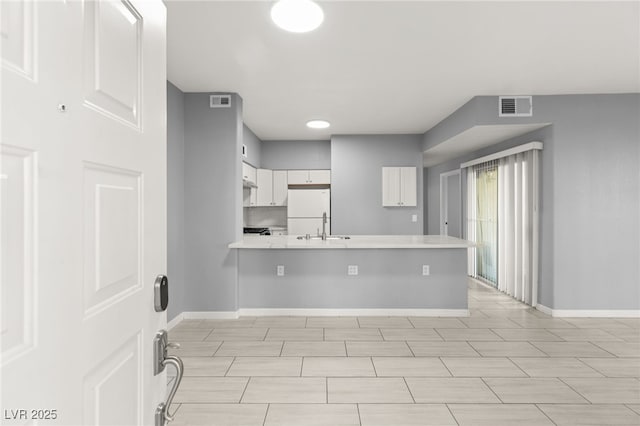 kitchen featuring a breakfast bar area, kitchen peninsula, white cabinets, and white fridge