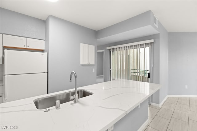 kitchen with light stone countertops, white fridge, white cabinets, and sink