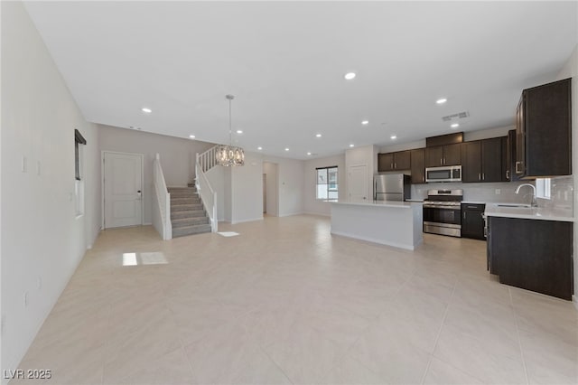 kitchen featuring dark brown cabinetry, sink, stainless steel appliances, decorative light fixtures, and a kitchen island