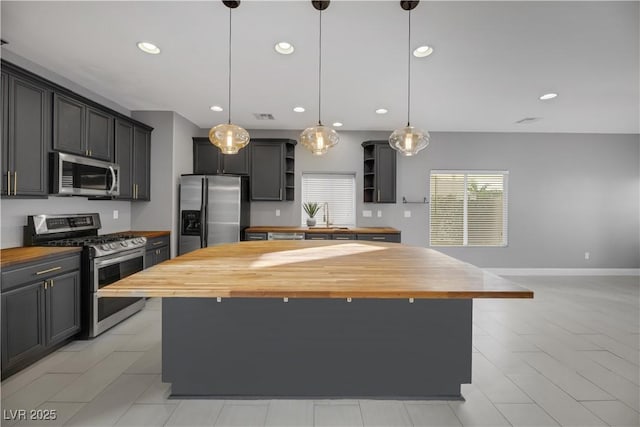 kitchen with butcher block counters, a center island, decorative light fixtures, and appliances with stainless steel finishes