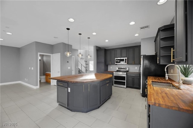 kitchen featuring a center island, wooden counters, hanging light fixtures, sink, and appliances with stainless steel finishes