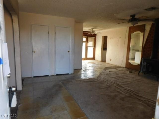 empty room with a wood stove, visible vents, and a ceiling fan