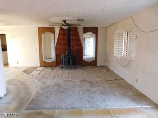 unfurnished living room featuring a wood stove, ceiling fan, visible vents, and a textured ceiling