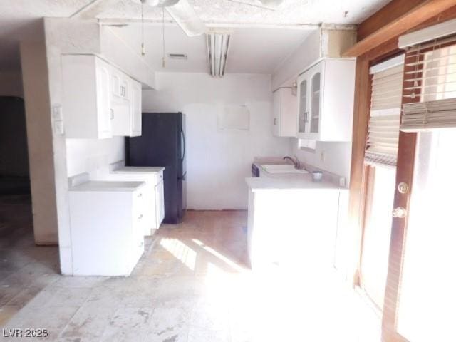 kitchen with light countertops, freestanding refrigerator, a sink, and white cabinetry