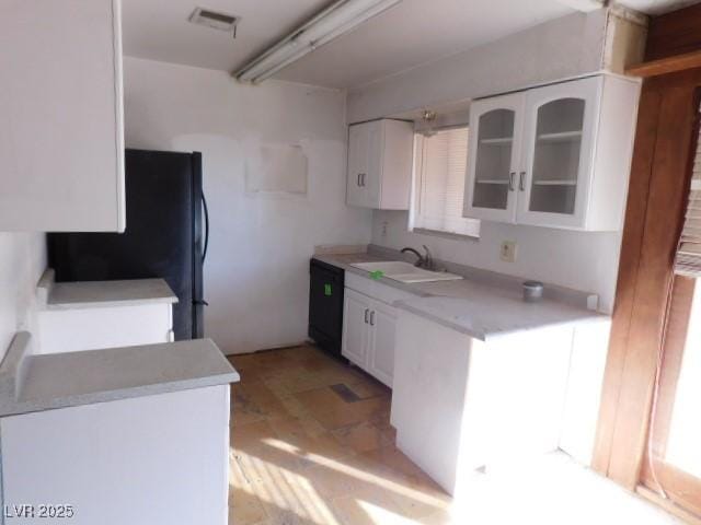 kitchen featuring visible vents, white cabinets, glass insert cabinets, light countertops, and a sink