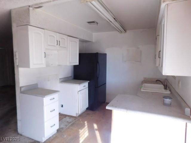 kitchen with light countertops, freestanding refrigerator, white cabinetry, and a sink