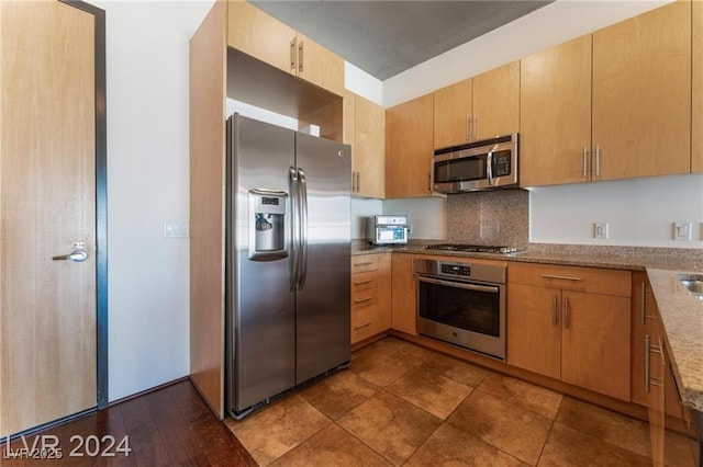 kitchen with light stone countertops, light brown cabinetry, backsplash, and stainless steel appliances