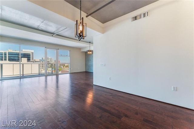 empty room with dark wood-type flooring and a notable chandelier