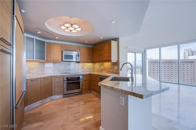 kitchen featuring sink, stainless steel appliances, light stone counters, kitchen peninsula, and a tray ceiling