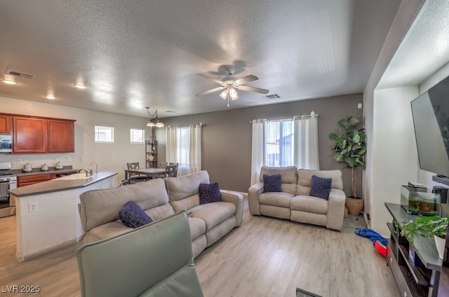 living room featuring ceiling fan with notable chandelier, a textured ceiling, and light hardwood / wood-style floors