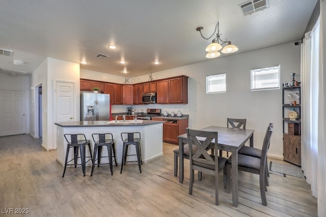 kitchen featuring sink, a notable chandelier, an island with sink, a textured ceiling, and appliances with stainless steel finishes