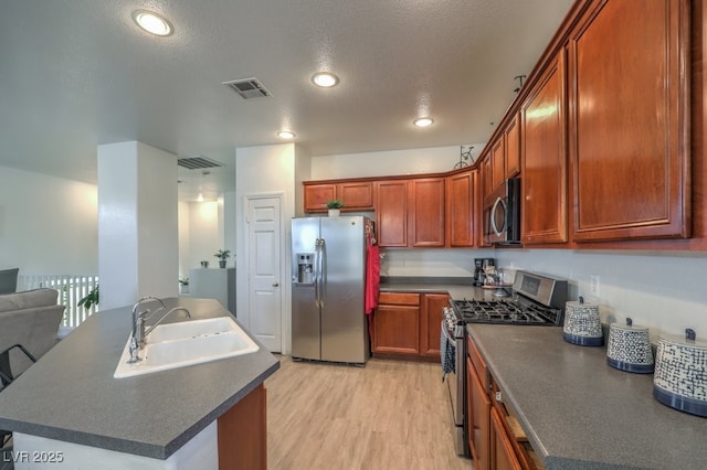 kitchen with a textured ceiling, sink, stainless steel appliances, and light hardwood / wood-style flooring