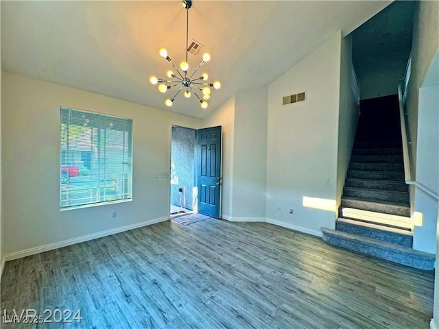 spare room with vaulted ceiling, hardwood / wood-style flooring, and an inviting chandelier