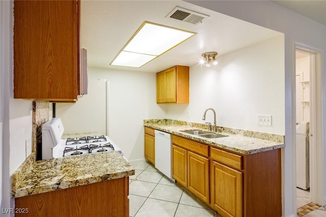 kitchen with white appliances, sink, light tile patterned flooring, light stone counters, and washer / clothes dryer