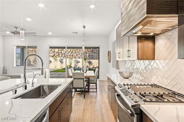 kitchen featuring decorative backsplash, premium range hood, gas range, sink, and decorative light fixtures