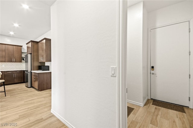 kitchen with dark brown cabinets, stainless steel fridge, decorative backsplash, and light hardwood / wood-style flooring