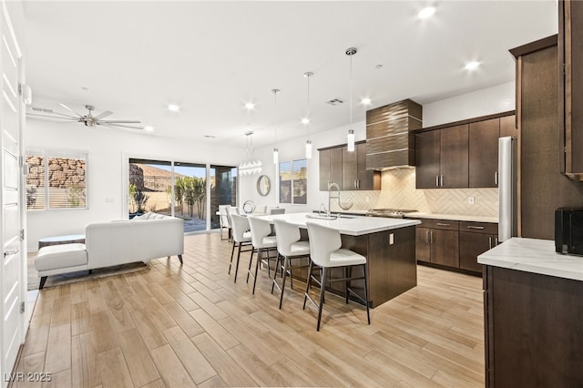 kitchen with open floor plan, wall chimney exhaust hood, light countertops, and dark brown cabinets