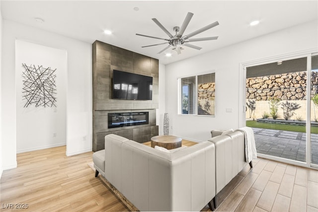 living area with ceiling fan, a fireplace, light wood-type flooring, recessed lighting, and baseboards